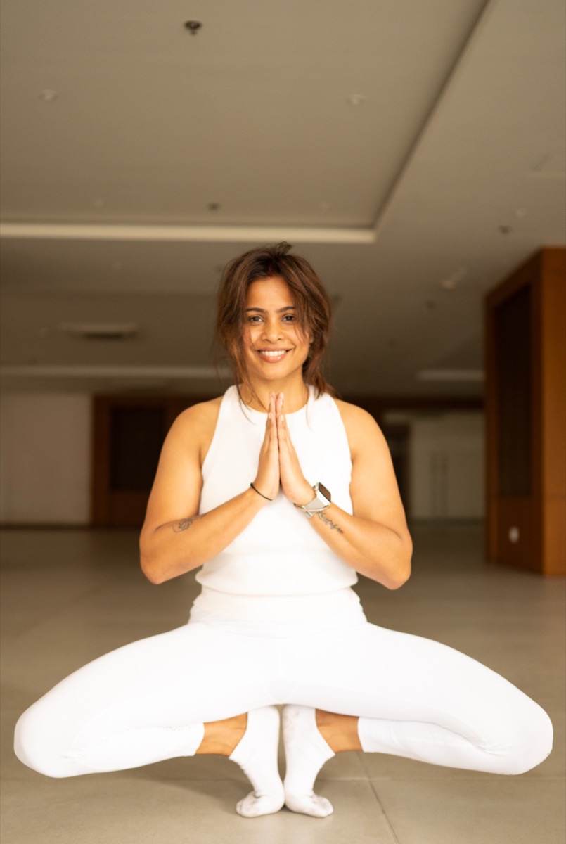 Nitu Singha, founder of Yogaikyam, smiling in a seated Hatha yoga pose with hands in prayer position
