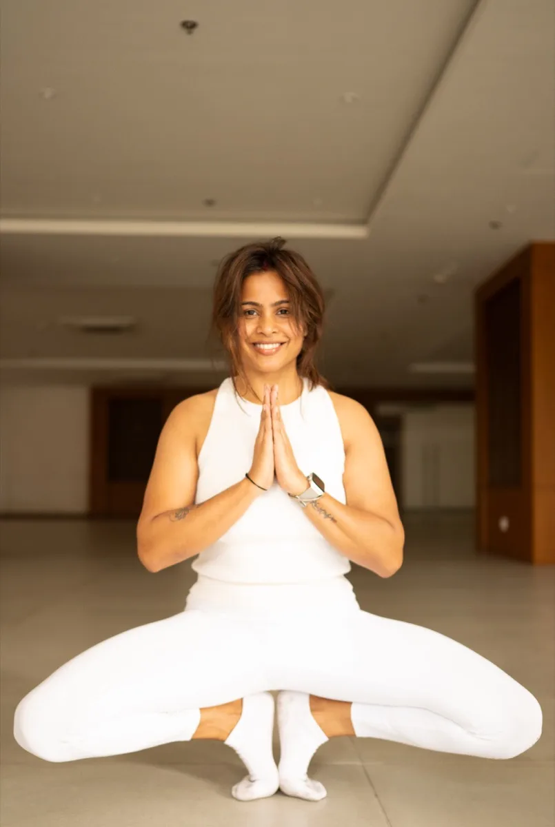 Nitu Singha, founder of Yogaikyam, smiling in a seated Hatha yoga pose with hands in prayer position